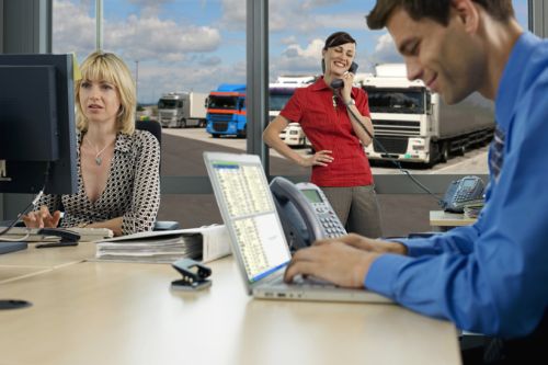 Three business people working in office, man using laptop, woman using PC, second woman using phone